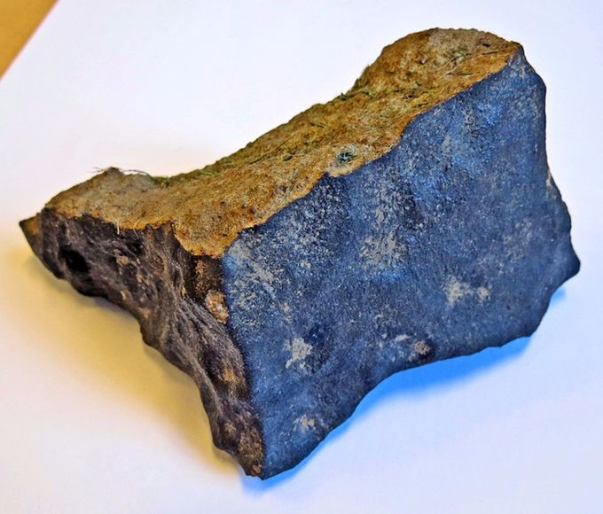 Den indleverede meteorit, der vejer godt 1/2 kg., ses her med tynd mørk smelteskorpe og et lysere indre. På meteoritten ses stadig lidt jord og græsstrå fra området, hvor den blev fundet.